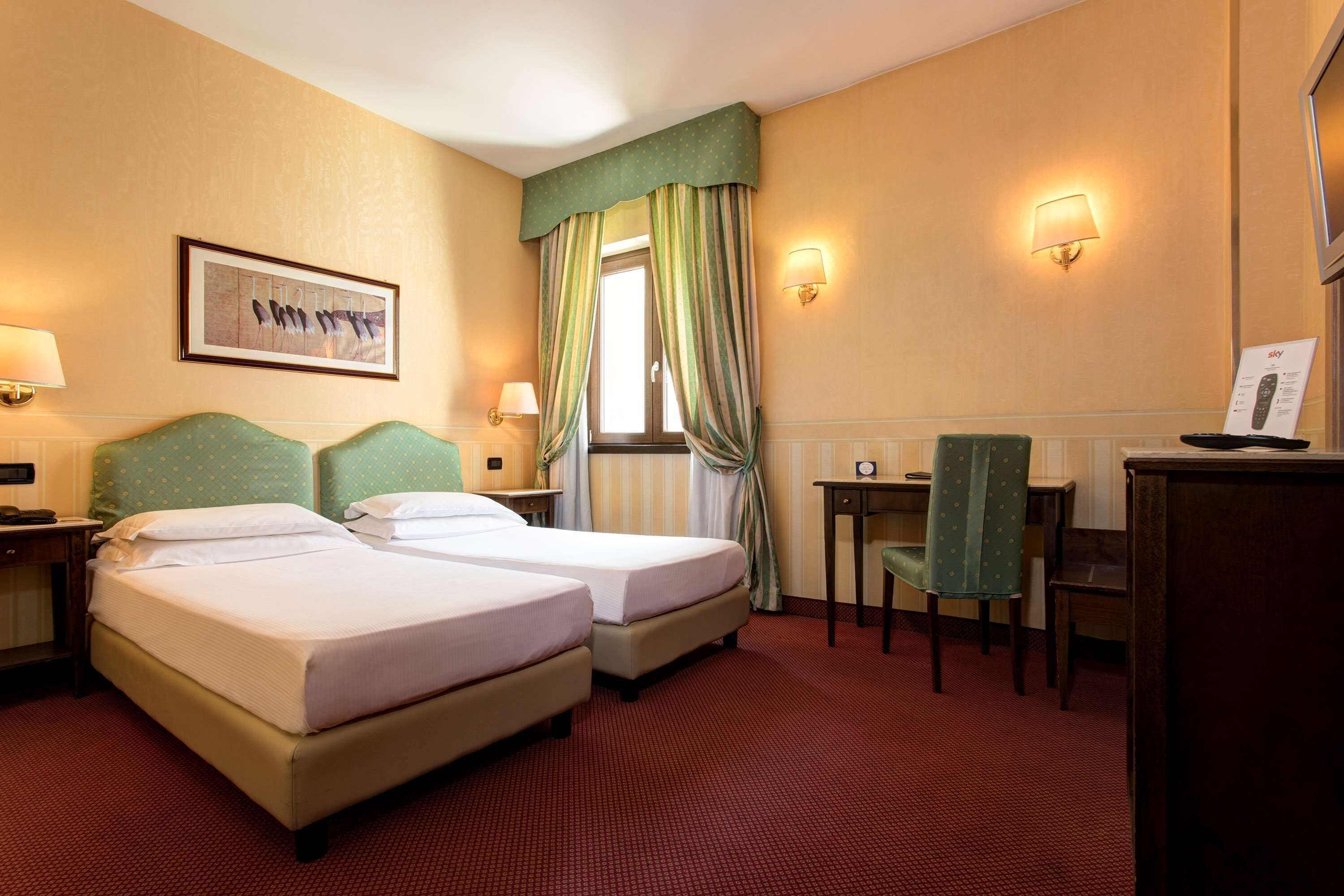 A hotel room with two beds, a desk, a chair, and a window with curtains.