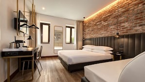 A modern hotel room with a brick wall, a bed, a desk with a chair, a television, and a large window. - Best Western Hotel Tritone (Mestre)