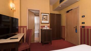 Ein Hotelzimmer mit Bett, Fernseher, Schreibtisch mit Fernbedienung, Stuhl, kleinem Tisch mit Wasserkocher und einer Tür.