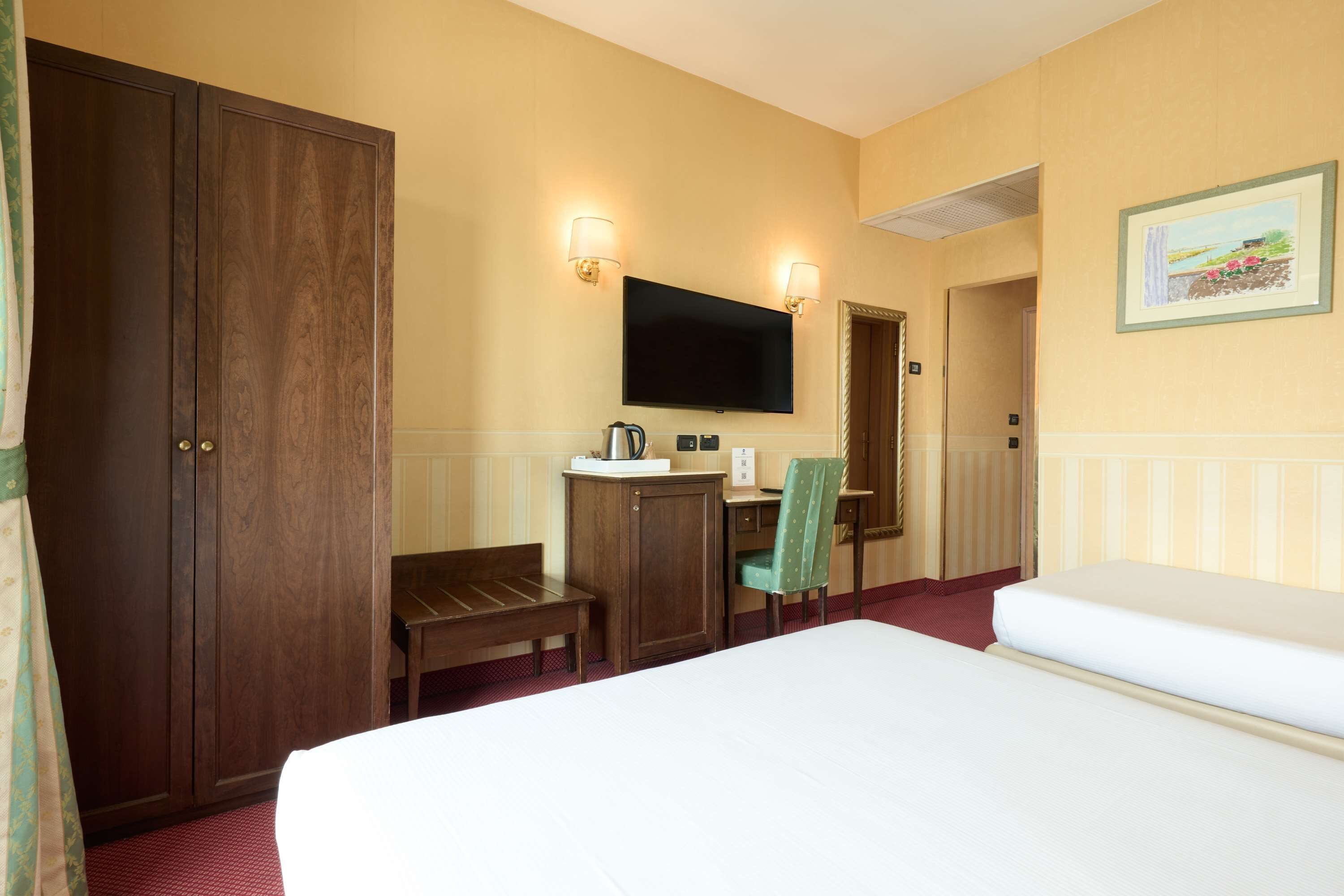 Una habitación de hotel con una cama grande, un escritorio con una silla, un televisor y un armario.