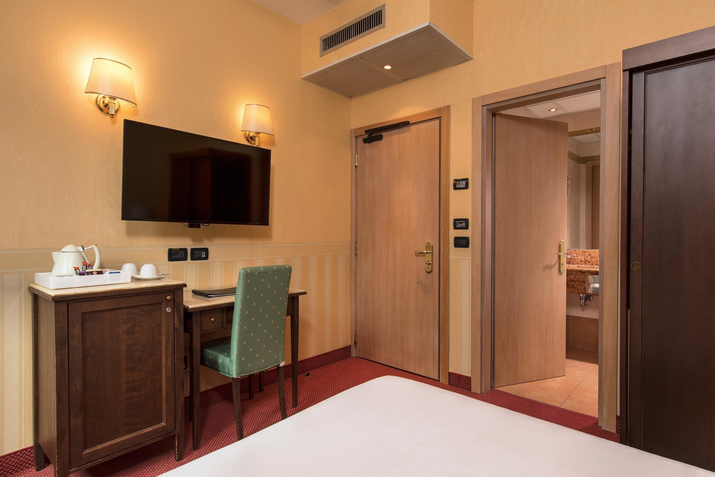 A hotel room with a bed, a desk with a chair, a television, and a door leading to a bathroom.