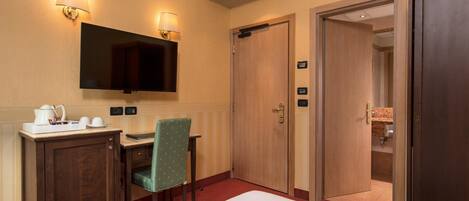 A hotel room with a bed, a desk with a chair, a television, and a door leading to a bathroom.