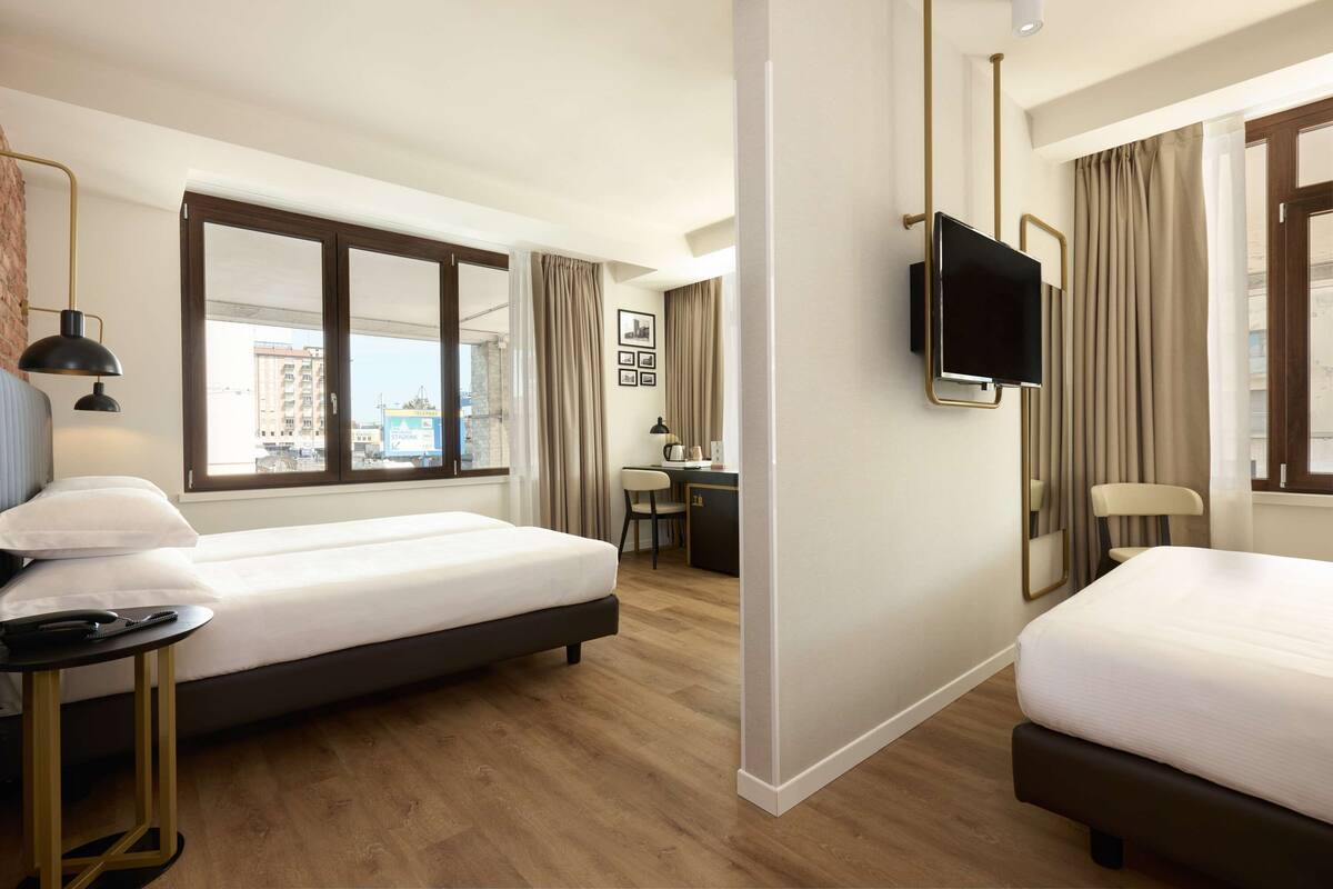 A hotel room with two beds, a desk, a chair, a TV, and a window with curtains.