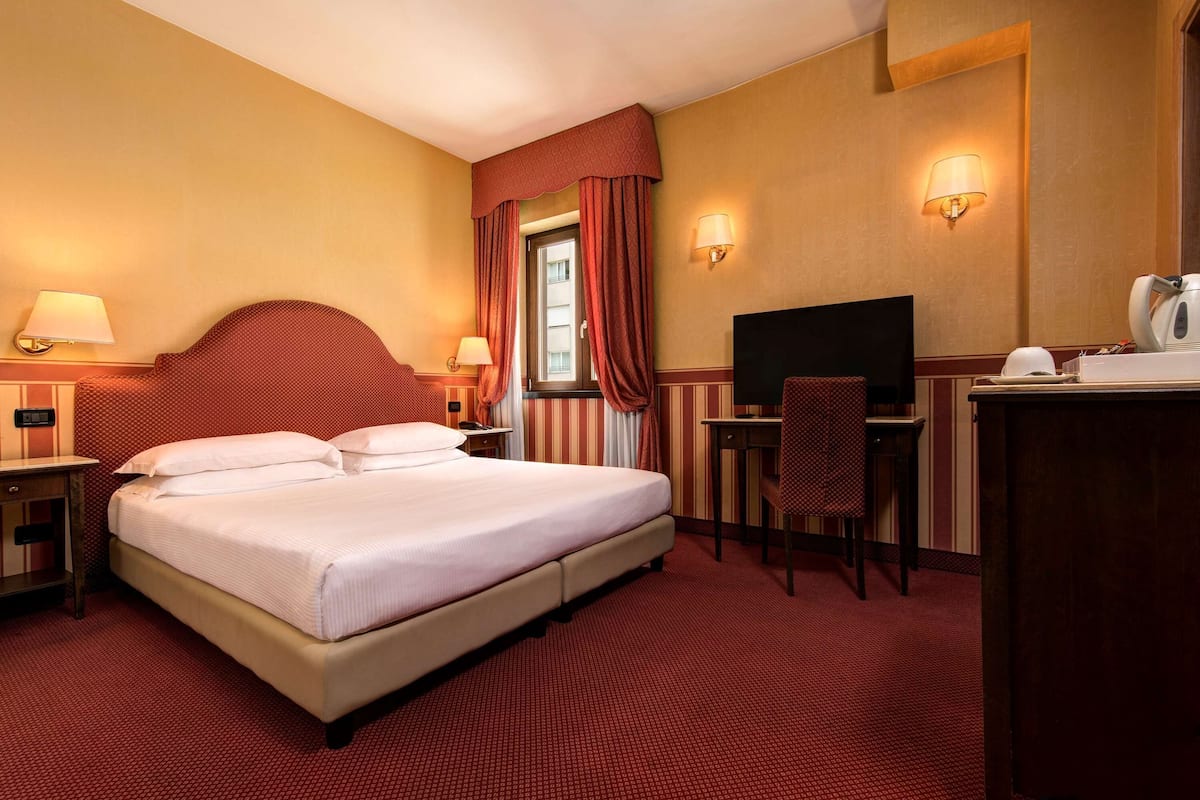 A hotel room with a large bed, a desk, a chair, a television, and a window with curtains.