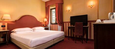 A hotel room with a large bed, a desk, a chair, a television, and a window with curtains.