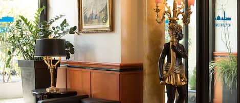A lobby with a statue, a framed painting, and a potted plant.