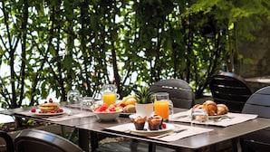 An outdoor dining table with breakfast items like pancakes, fruit, and croissants, surrounded by chairs and a potted plant. - Best Western Hotel Tritone (Mestre)