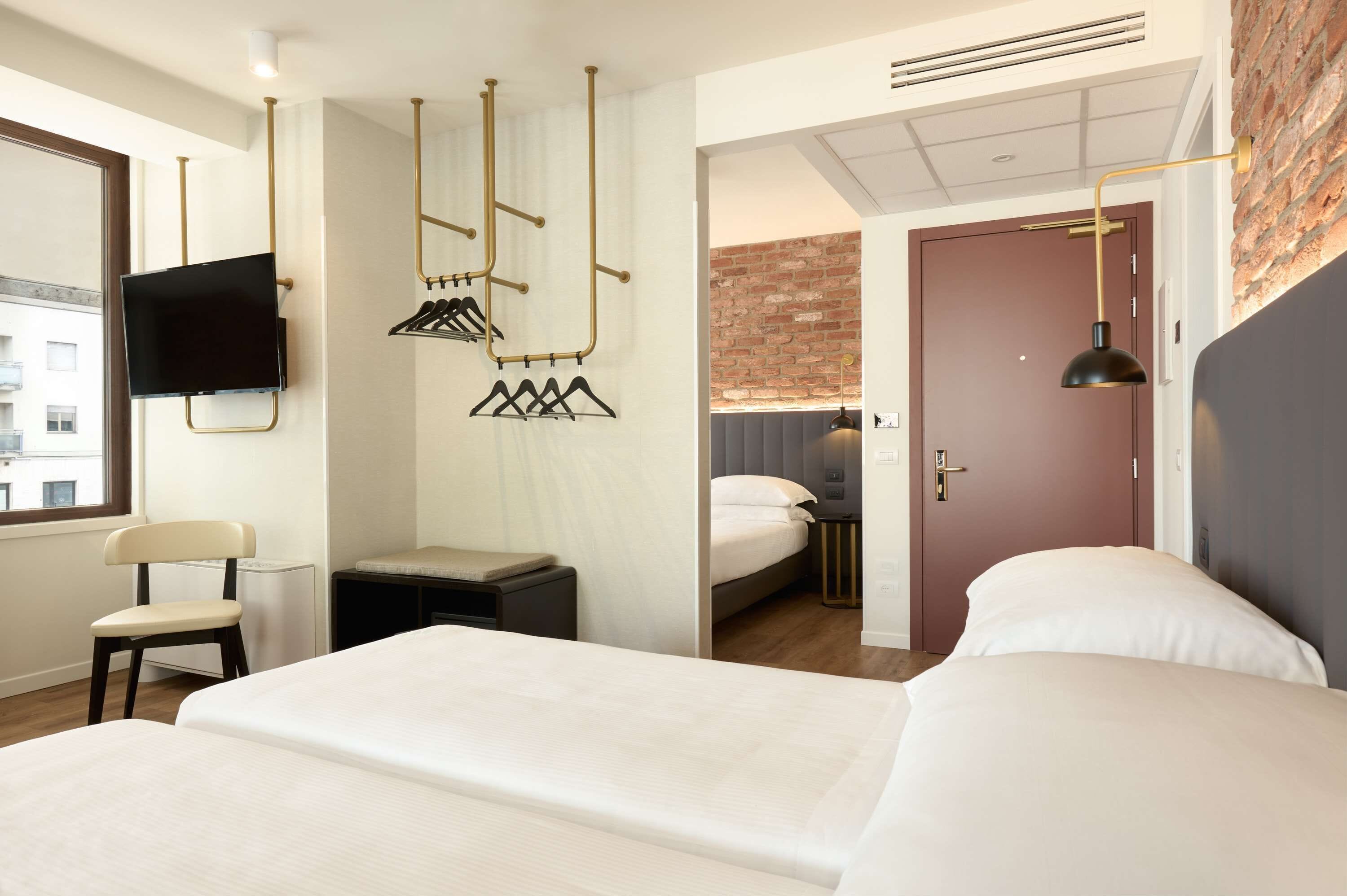 A modern hotel room with a large bed, a TV mounted on the wall, a chair, and a desk with a lamp.
