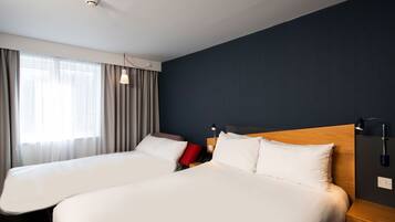 A hotel room with two beds, a window with curtains, and a wall-mounted lamp.