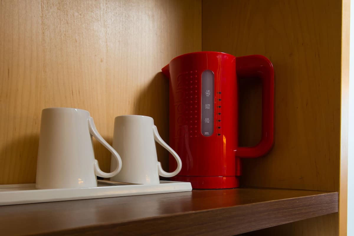 A shelf with two white mugs and a red coffee maker.