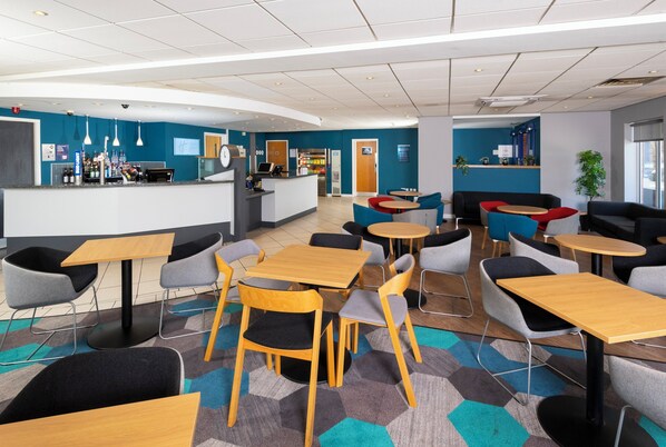 A modern cafe with multiple seating options, including tables and chairs, and a counter area with a beverage display.
