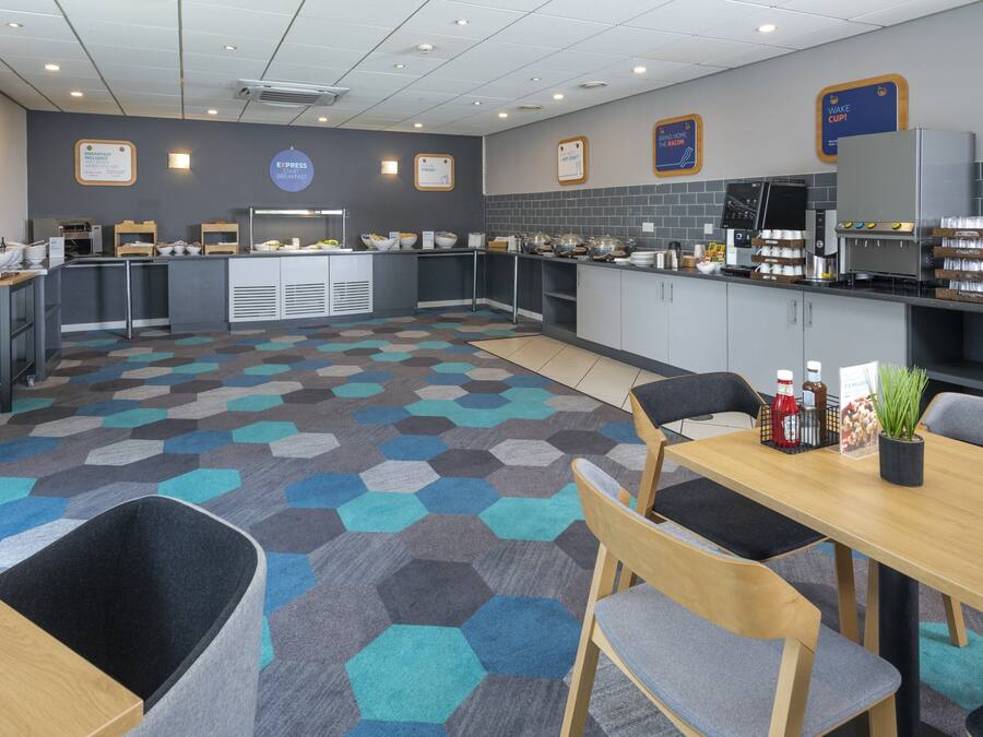 A modern breakfast area with a hexagonal patterned floor, a central island with food and beverage dispensers, and seating arrangements.