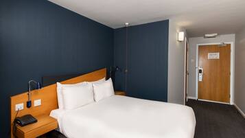 Habitación de hotel con una cama grande, un cabecero de madera, una mesita de noche con un teléfono y otra mesita de noche.
