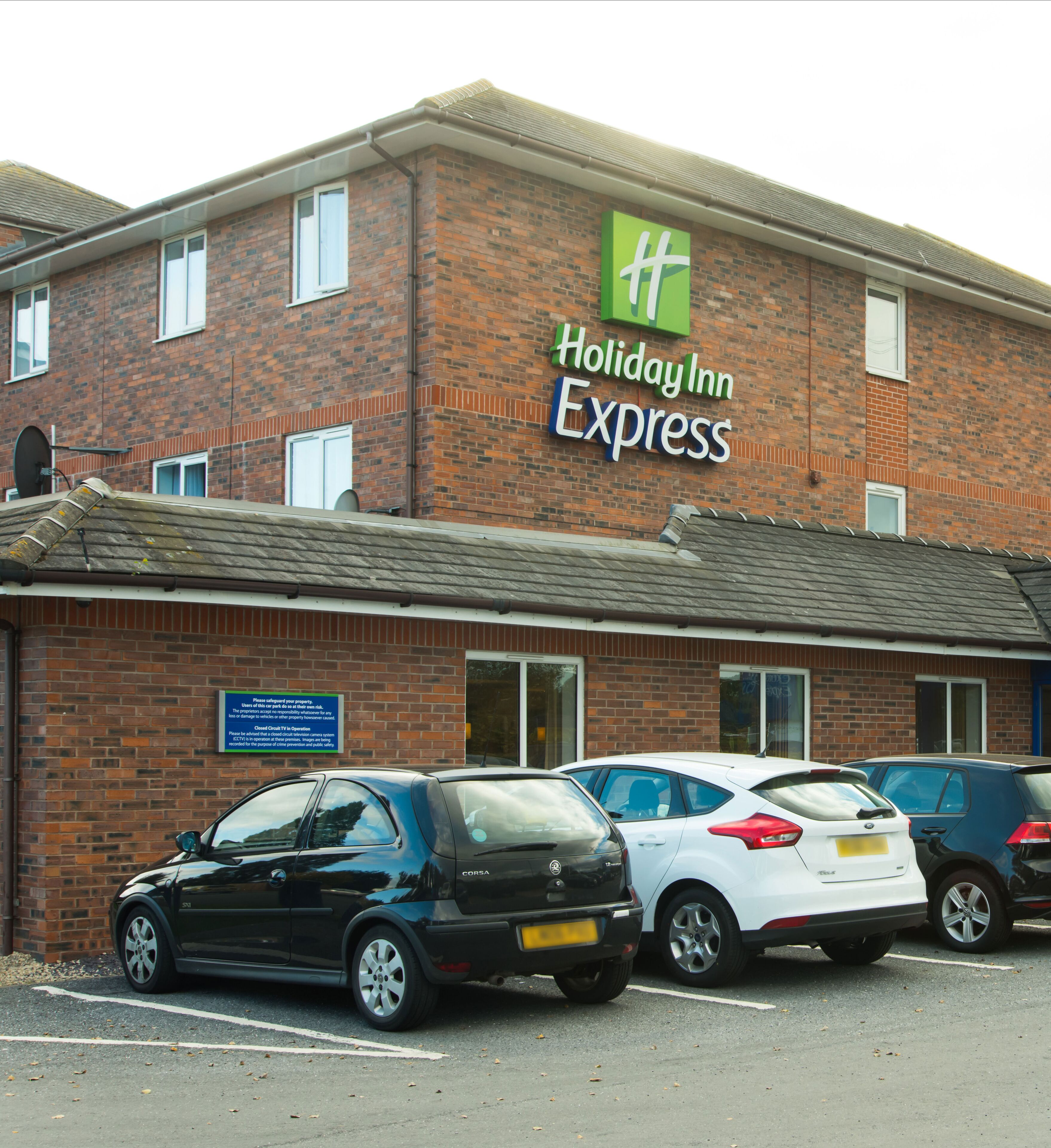 A Holiday Inn Express building with a brick facade, multiple windows, and a sign indicating its name. There are several cars parked in front.