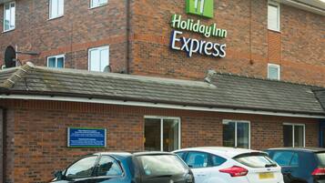 A Holiday Inn Express building with a brick facade, multiple windows, and a sign indicating its name. There are several cars parked in front.