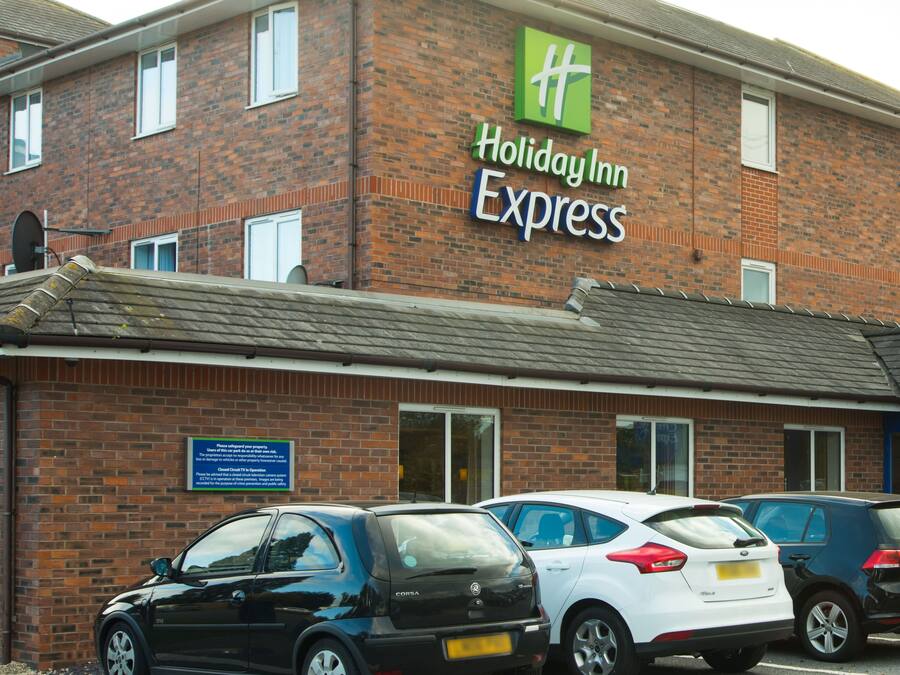 A Holiday Inn Express building with a brick facade, multiple windows, and a sign indicating its name. There are several cars parked in front.