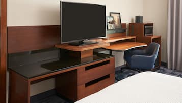 Habitación de hotel con una cama grande, un escritorio de madera con televisor de pantalla plana, una silla azul, microondas y un armario pequeño.