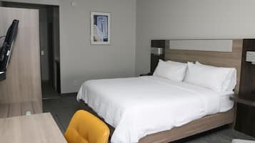 Quarto de hotel com uma cama grande, uma escrivaninha, uma cadeira e uma televisão.