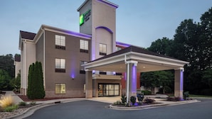 Ein Hotel mit auffälliger Beschilderung, einem überdachten Eingangsbereich und einer angelegten Grünfläche mit Bäumen und Sträuchern.