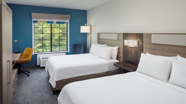 A hotel room with two beds, a desk, a chair, a window with a view of trees, and a wall-mounted lamp. - Holiday Inn Express & Suites Albermarle by IHG (Albemarle)