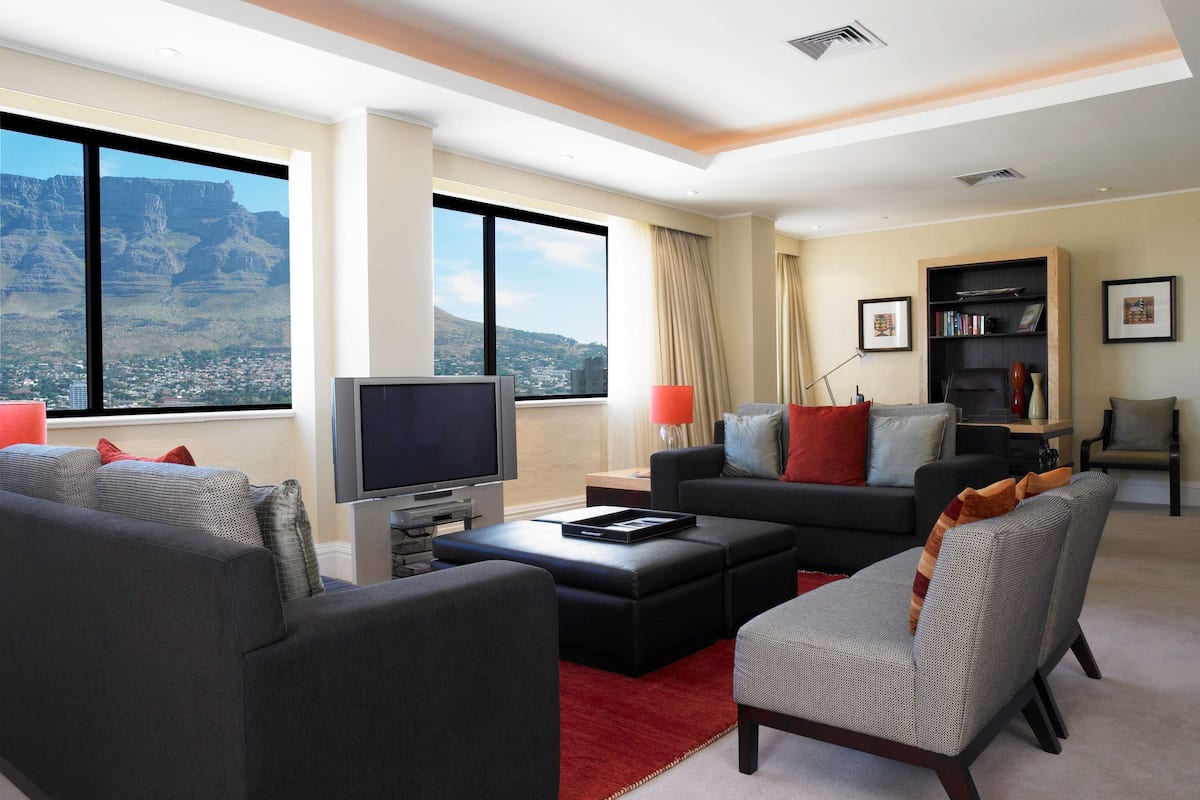A modern living room with a large window, a flat-screen TV, a sofa, a coffee table, and a bookshelf.