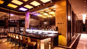 Uma área de bar com um balcão comprido, vários bancos e uma parede decorativa.