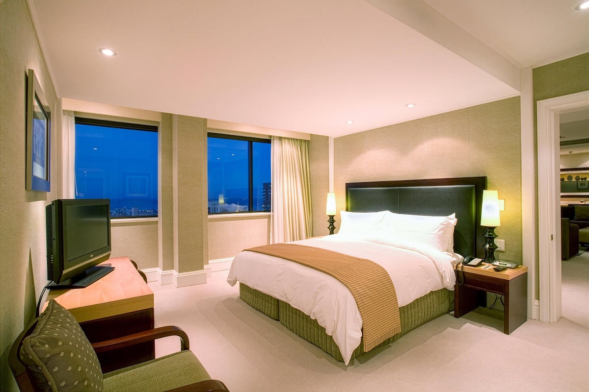 A hotel room with a bed, a desk with a computer, a chair, a TV, and a view of the city at night.
