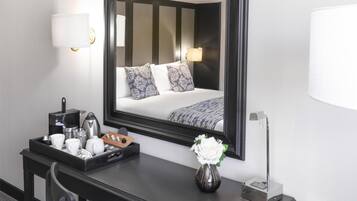 Camera d'albergo con uno specchio grande, una scrivania con un vassoio per la colazione, un vaso con un fiore e un letto con cuscini decorati.