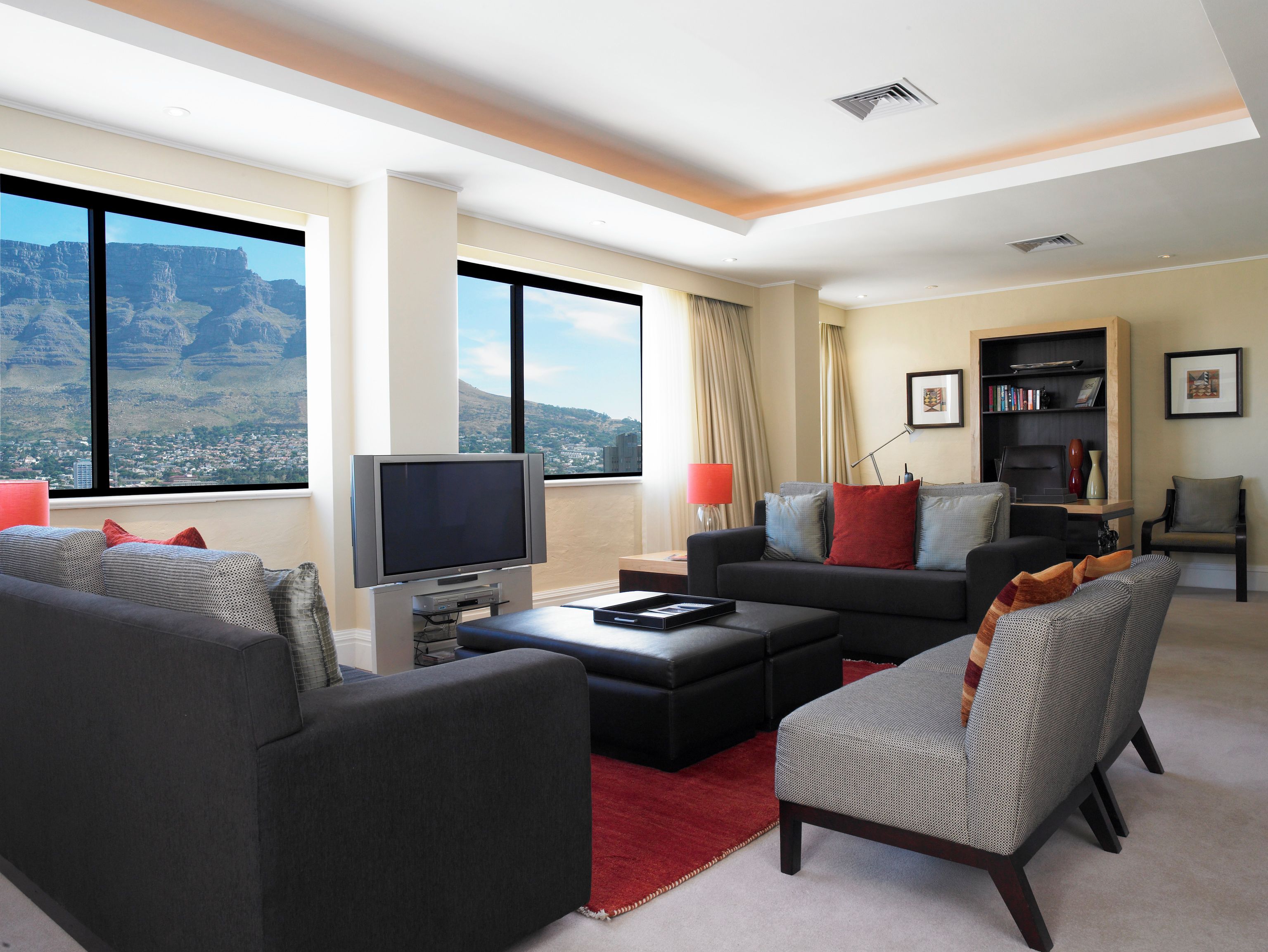 A modern living room with a large window, a flat-screen TV, a sofa, a coffee table, and a bookshelf.