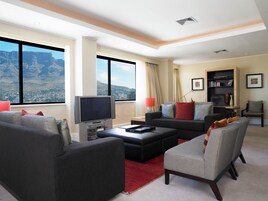 A modern living room with a large window, a flat-screen TV, a sofa, a coffee table, and a bookshelf.