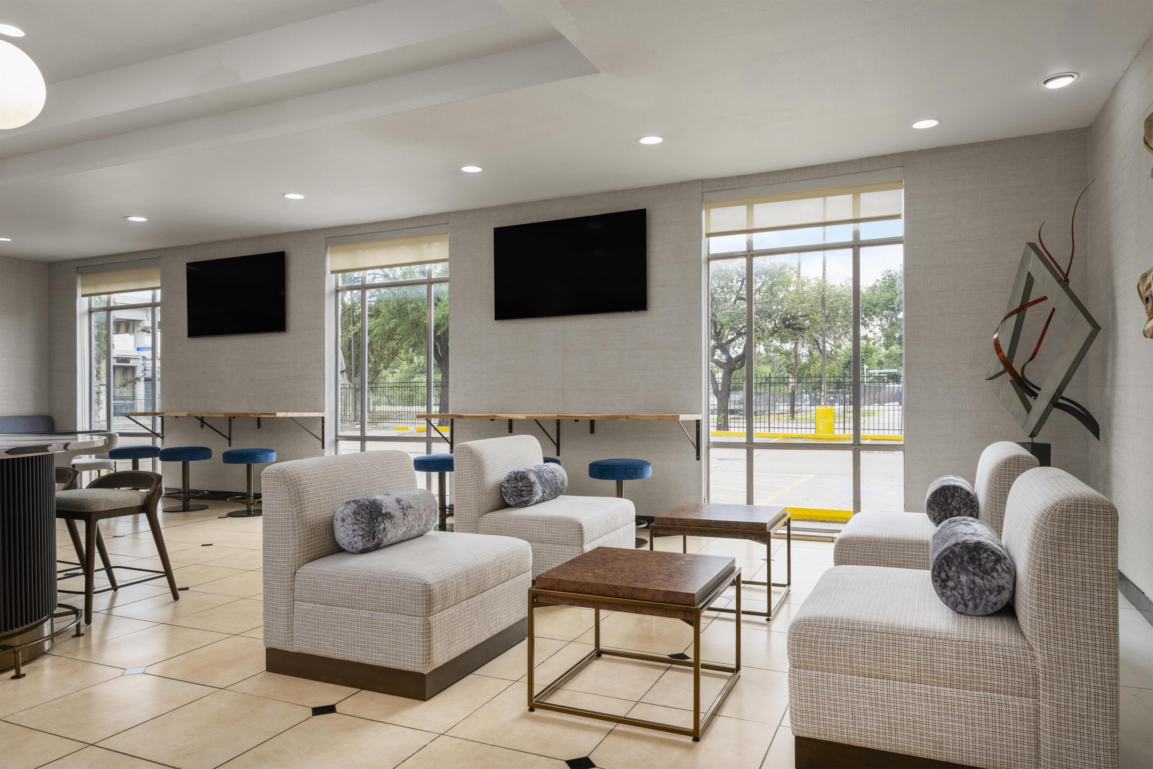 A modern hotel lobby with seating areas, a flat-screen TV, and large windows.