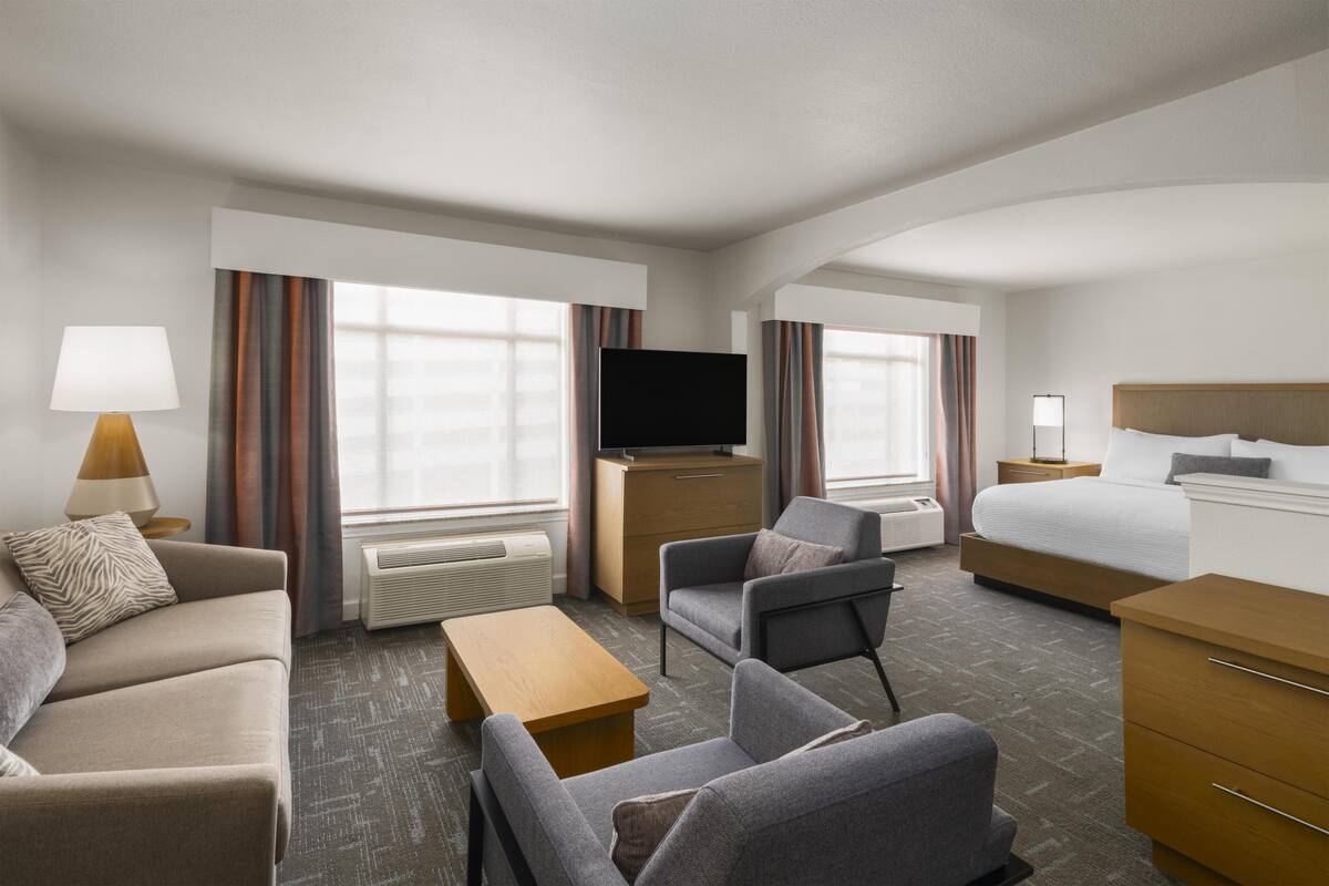 A hotel room with a sofa, armchair, bed, TV, and a desk.