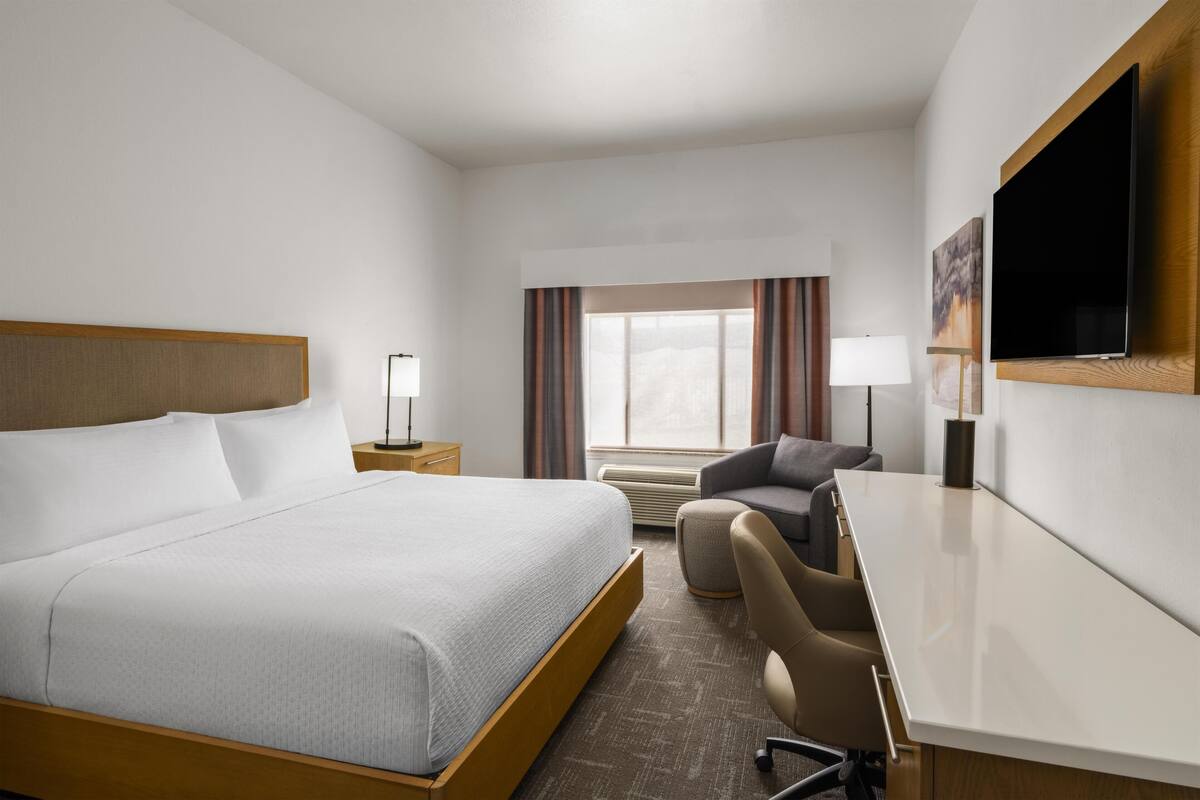A hotel room with a bed, a desk, a chair, a TV, and a window with curtains.