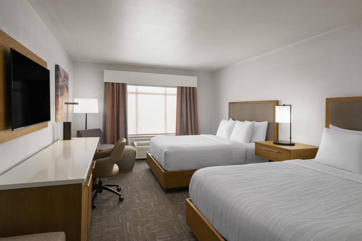A hotel room with two beds, a desk, a chair, a TV, and a window with curtains.
