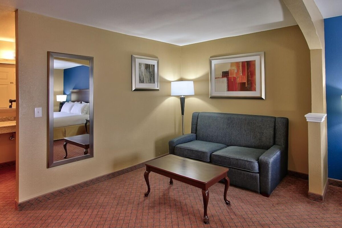 Una camera d'albergo con un letto, una poltrona, un tavolino, una lampada e opere d'arte alle pareti.