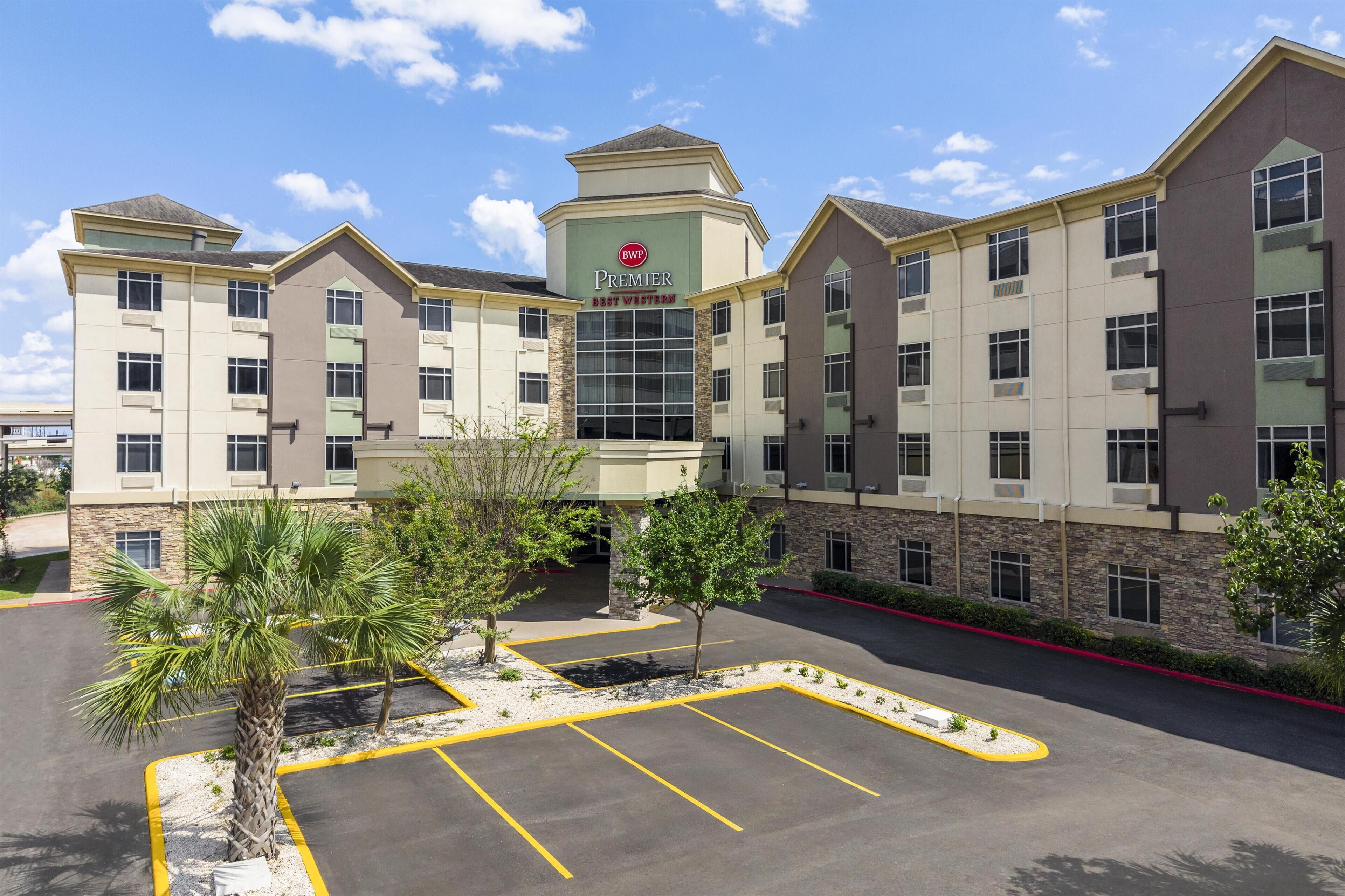 A multi-story hotel with a prominent sign, a parking lot with marked spaces, and a landscaped area with trees.