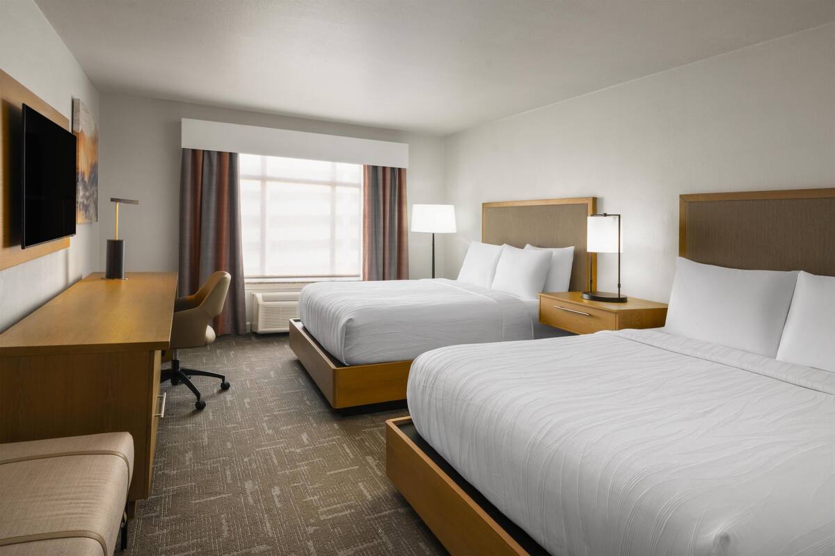 A hotel room with two beds, a desk, a chair, a TV, and a window with curtains.