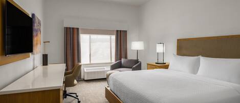 Une chambre d’hôtel équipée d’un lit, d’un bureau, d’une chaise, d’une télévision, d’une lampe et d’une fenêtre avec des rideaux.