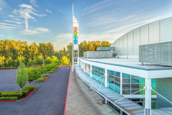 A modern building with a large glass facade, a prominent flagpole with the letters "expo," and a parking lot with neatly trimmed trees. - Holiday Inn Express Hotel & Suites Portland-NW Downtown by IHG (Portland)