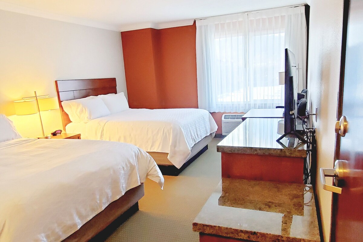 A hotel room with two beds, a desk with a computer, and a window with curtains.