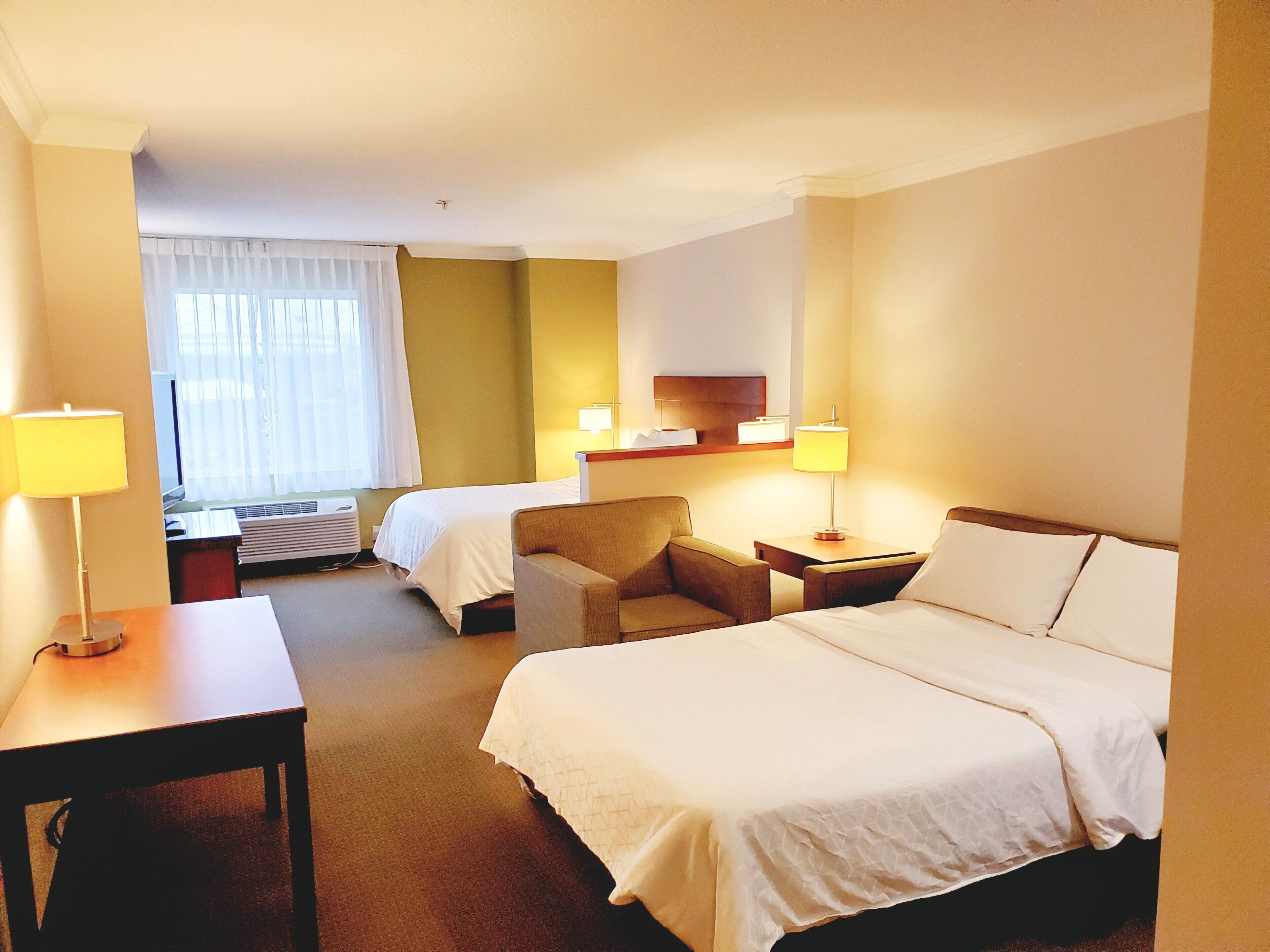 Ein Hotelzimmer mit zwei Betten, einem Schreibtisch, einem Stuhl und einem Fenster mit Vorhängen.