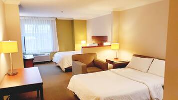 Ein Hotelzimmer mit zwei Betten, einem Schreibtisch, einem Stuhl und einem Fenster mit Vorhängen.