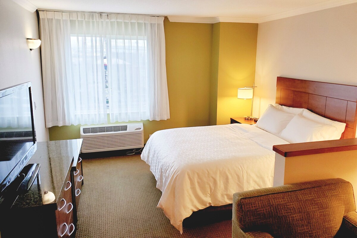 A hotel room with a bed, a desk with a computer, a chair, a lamp, and a window with curtains.