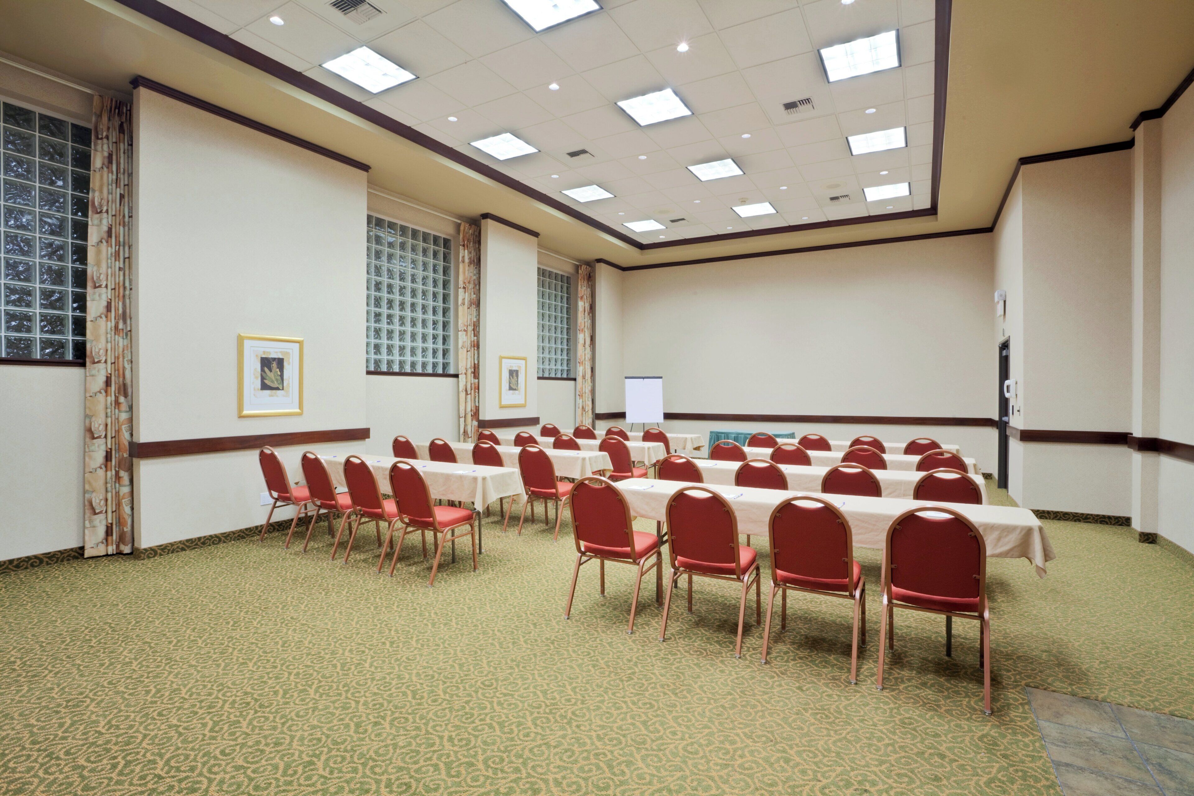 A conference room with multiple tables and chairs, large windows with curtains, and a whiteboard.