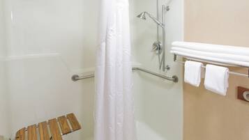 A shower area with a glass door, a wooden bench, and a towel rack with towels.
