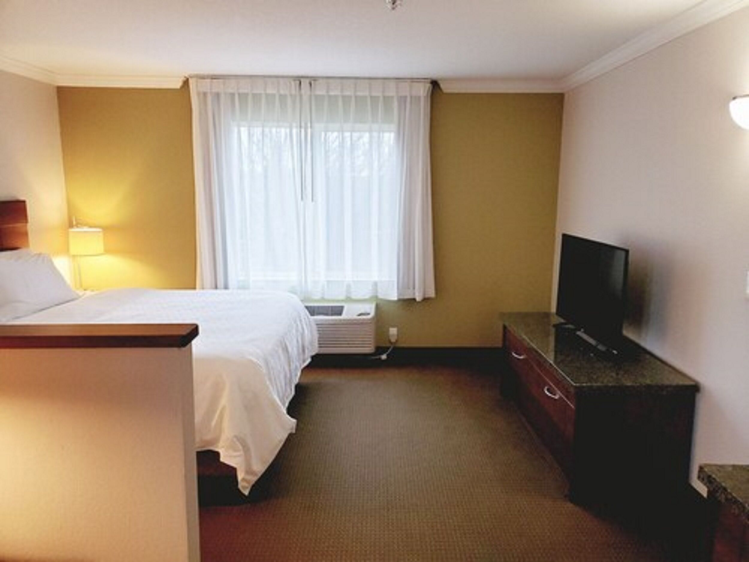 Ein Hotelzimmer mit Bett, Fernseher, Schminktisch und einem Fenster mit Vorhängen.