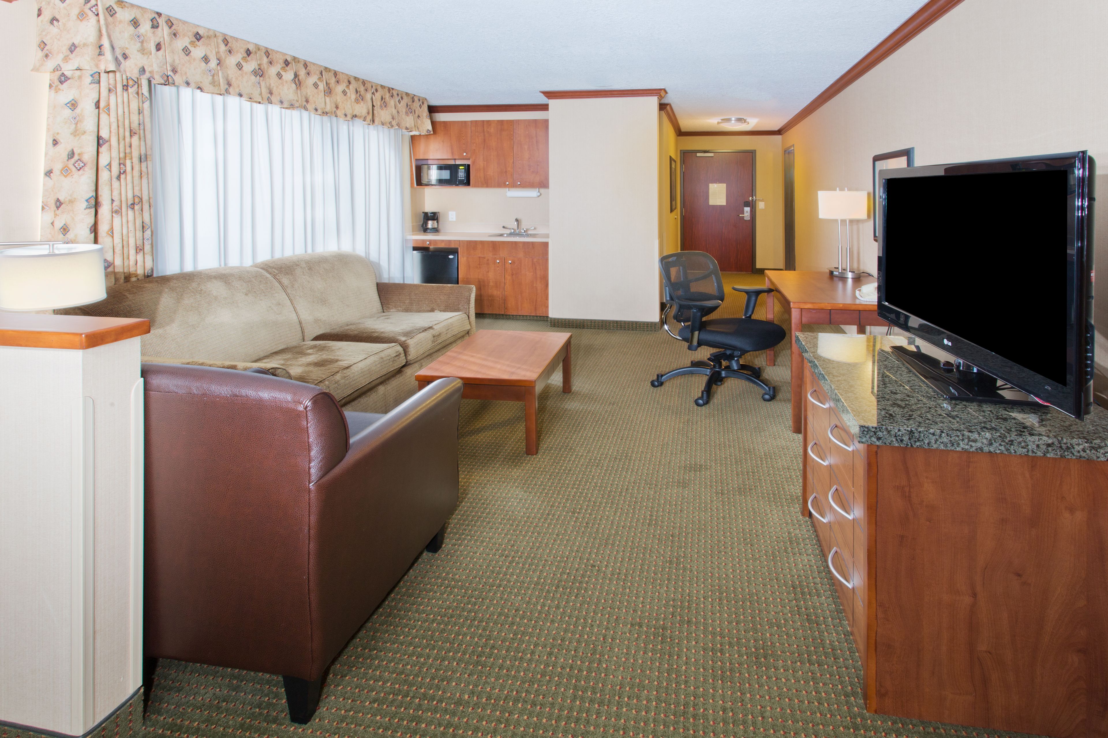 Une chambre d’hôtel compacte comprenant un canapé, une petite table, un téléviseur, un bureau et une kitchenette.