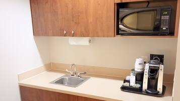 A compact kitchen with wooden cabinets, a microwave, a coffee maker, and a dishwasher.