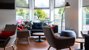 A modern interior with a sofa, chairs, a small table, and large windows offering a view of the street. - Holiday Inn Express Swindon - West by IHG (Swindon)