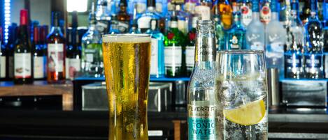 A bar counter with two glasses of beer and a bottle of tonic water.